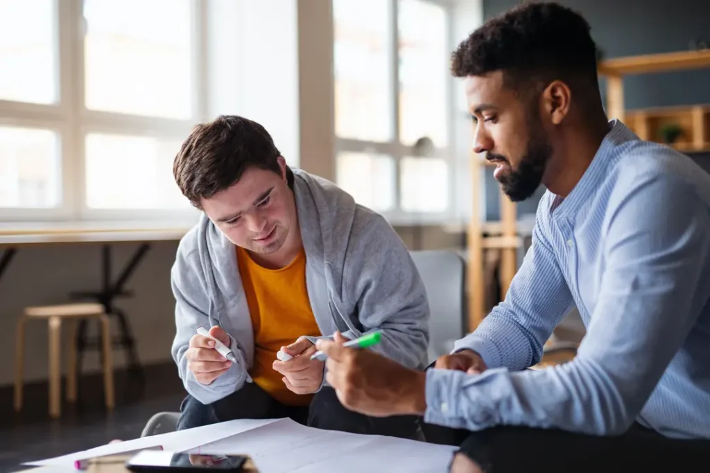 Young man either Down syndrome and his male support worker looking over paperwork