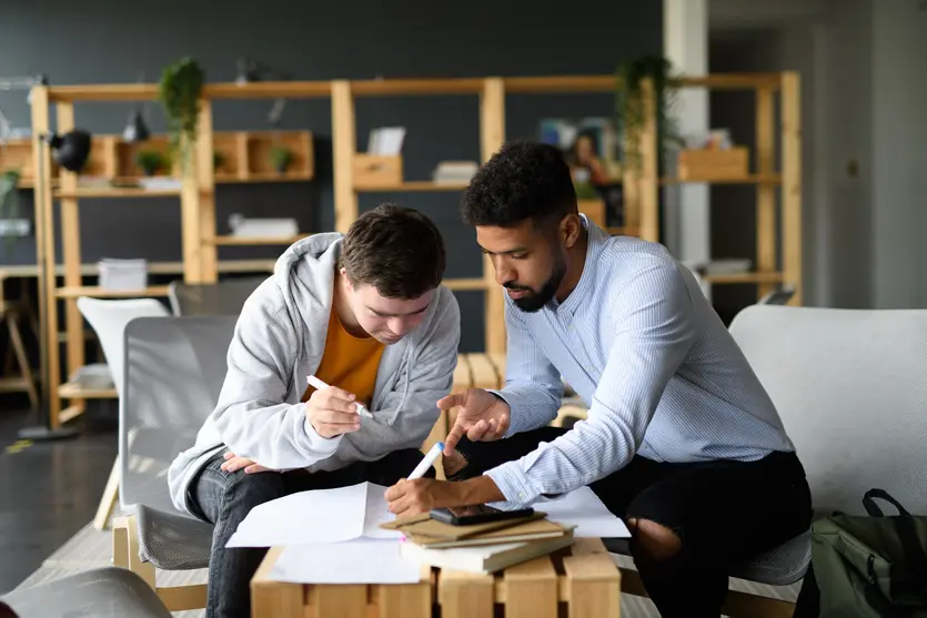 young man with Down syndrome and his male support worker sitting on a lounge looking over paperwork as part of his support coordination